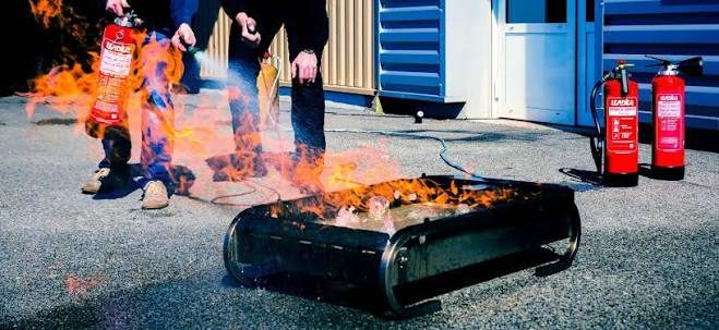 Dos personas apagan con extintores un fuego en una bandeja durante una práctica al aire libre.
